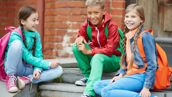 Three school children sitting on steps with their backpacks.