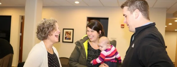 Three adults talking and one adult holding baby