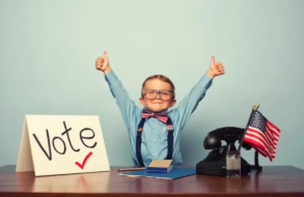 A child giving a thumbs up in front of a "Vote" sign