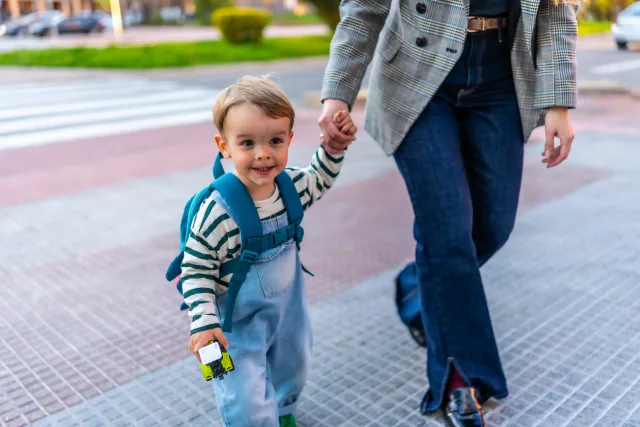 mom holding onto childs hand while walking into childcare